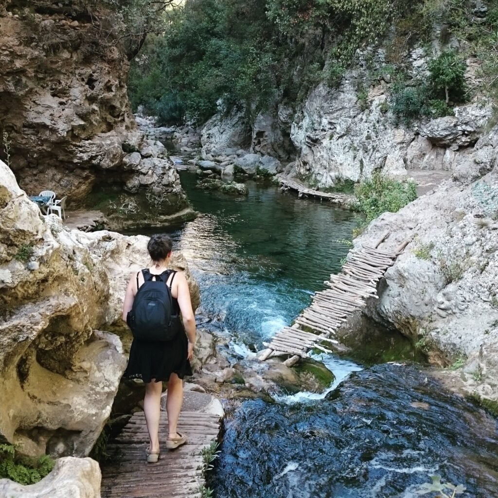 A hiker with a backpack walks along a wooden path beside the river at Akchour
