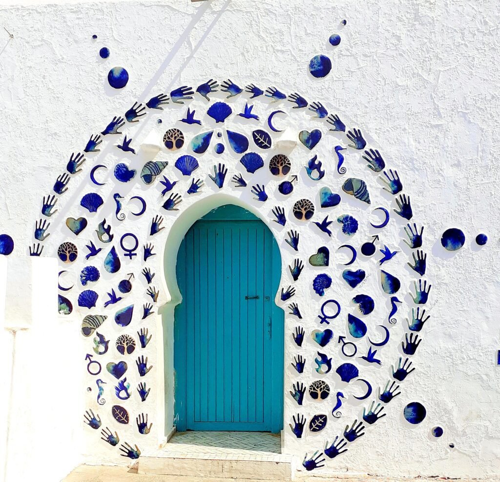 A blue door framed by hand-shaped ceramic decorations on a white wall in Asilah, one of the Asilah murals