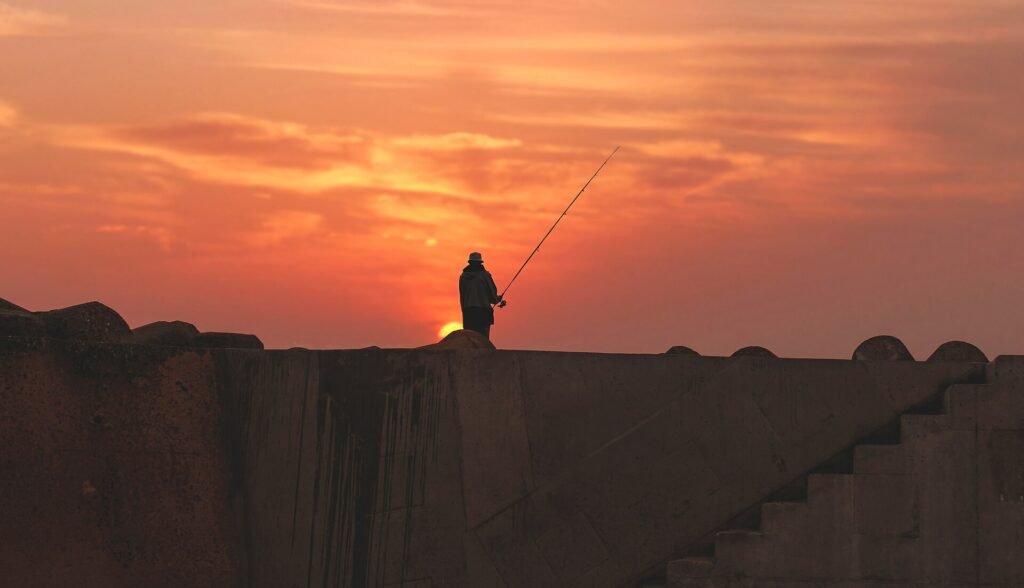 A fisherman standing on the walls of Asilah against an orange sunset sky