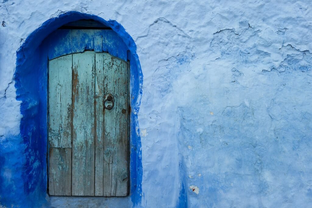 Why is Chefchaouen blue? A blue wooden door in a wall painted in several shades of blue in the blue city of Morocco