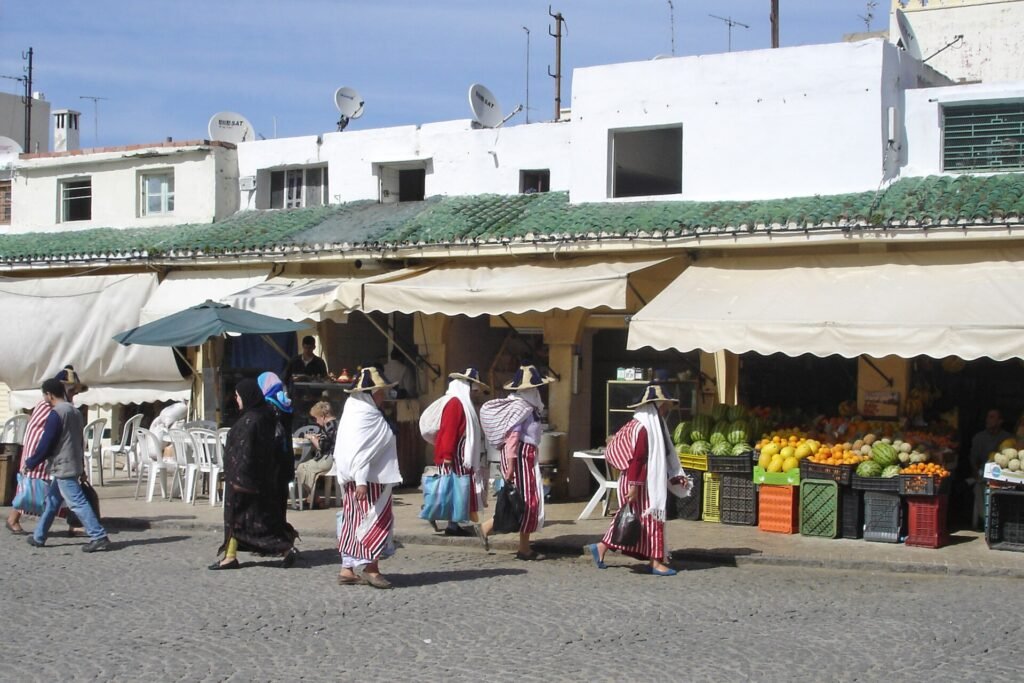 Women in traditional striped clothes walking past fruit stalls on the Grand Socco of Tangier