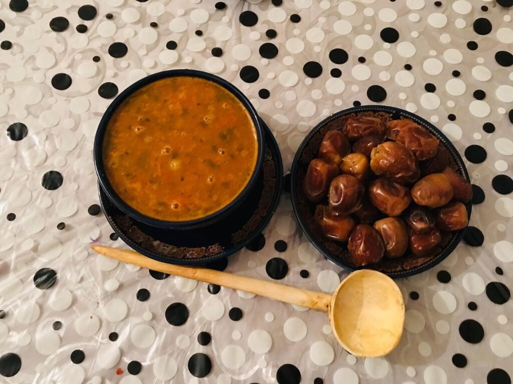 A bowl of harira soup next to a plate of dates and a wooden ladle