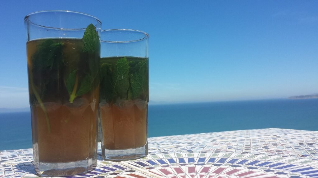 Two glasses of mint tea on a tiled table with the sea behind