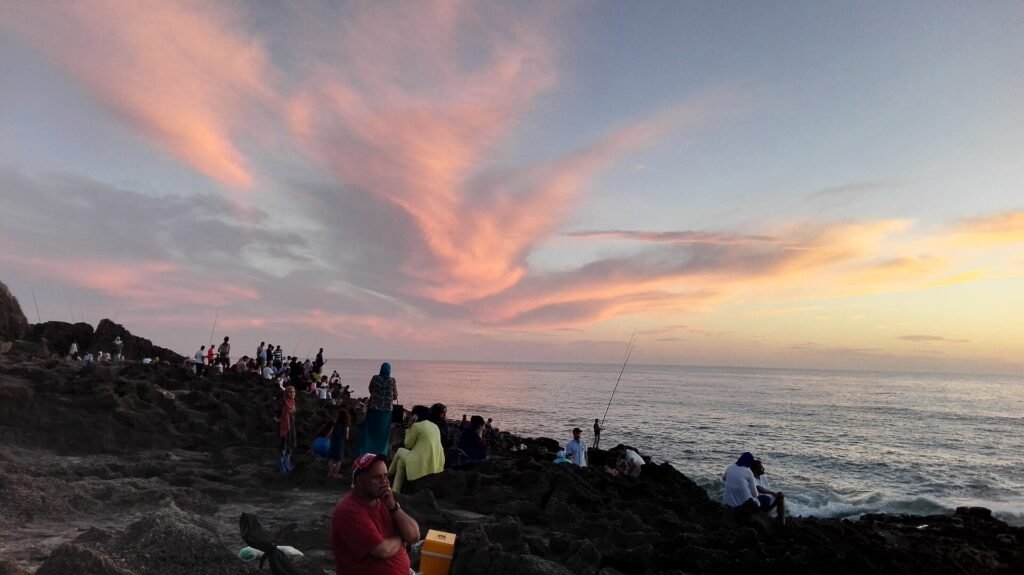 People on the rocks of the Tangier coast watching a pink sunset over the Atlantic