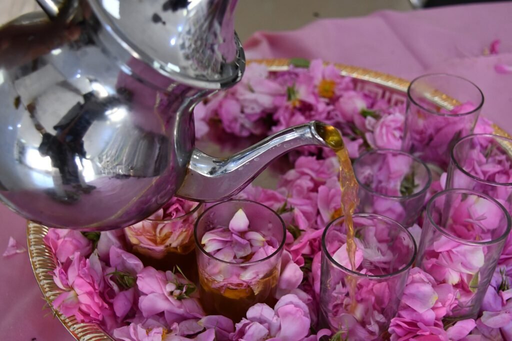 A silver teapot pouring mint tea into glasses among pink rose petals, a sign of Moroccan culture and etiquette